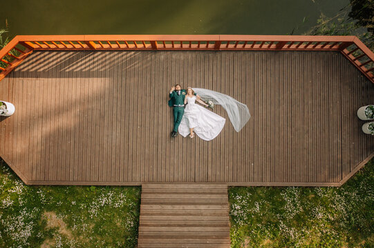 Bride and groom are lying on a jetty on the shore of a lake. Wedding couple. Happy family. A man and a woman in love. Aerial view. Shot from a drone