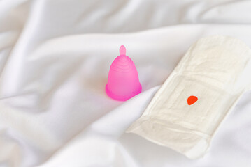 Reusable menstrual cup and  sanitary napkins on white cloth, concept female intimate hygiene period products and zero waste. Minimalism.  Copy space.