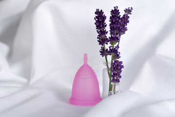 Reusable menstrual cup and lavender  on white cloth, concept female intimate hygiene period products and zero waste. Minimalism.