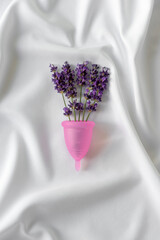 Reusable menstrual cup and lavender  on white cloth, concept female intimate hygiene period products and zero waste. Minimalism.
