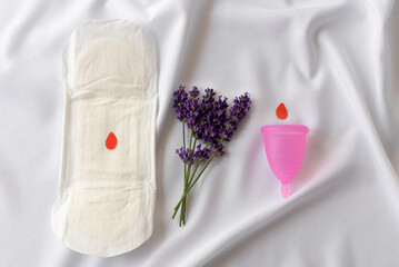 Reusable menstrual cup, lavender and  sanitary napkins on white cloth, concept female intimate hygiene period products and zero waste. Minimalism. Copy spase.