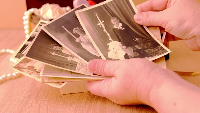female hands are sorting dear to heart memorabilia in an old wooden box, stack of retro photos, vintage photographs of 1960, concept of family tree, genealogy, childhood memories, home archive