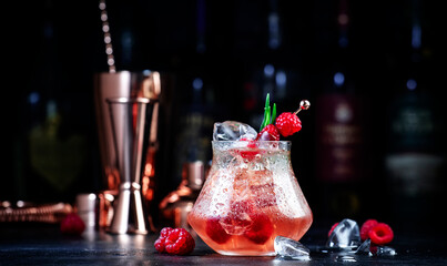 Pink rum alcoholic cocktail drink with white rum, pineapple juice, cranberries, raspberries and ice. Black bar counter background, bar tools and bottles - obrazy, fototapety, plakaty
