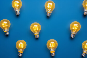 Overhead flat lay view of a collection of glowing yellow light bulbs on a blue background