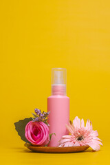 Obraz na płótnie Canvas Floral style of showcase for cosmetics product display on yellow background with flowers. Pink bottle cosmetics product with flowers