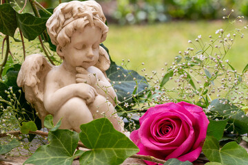 Kleine Engelsfigur mit rosafarbener Rose im Garten
