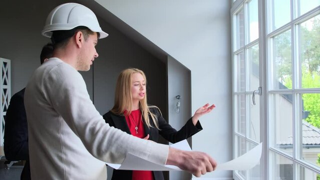 Professional builder shows blueprint of summer cottage residence to wealthy couple. Architect shares details of planned renovation