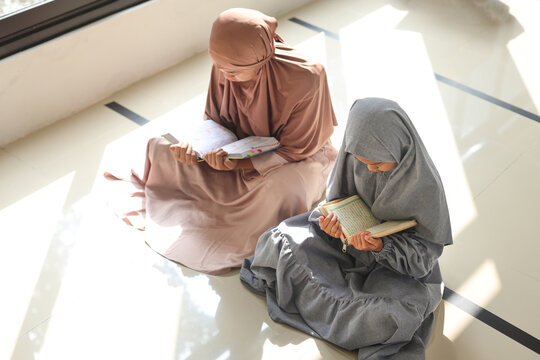 Two little Muslim girls reading Quran Holy Book near window of the mosque, top view 