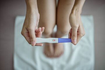 Close-up of young woman holds a pregnancy test in her hands. Positive pregnancy test. © Thanumporn