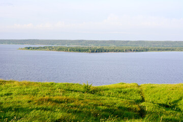 Fototapeta premium lakeshore on the sunset with green grass and blue water and horizon, copy space