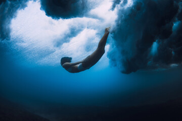 Surfer girl dive underwater with ocean powerful and dangerous wave.