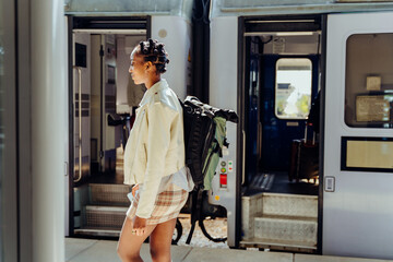 African american traveler woman with luggage getting off the train at train station platform. Ready for an adventure trip through Europe alone as a nomadic backpacker.