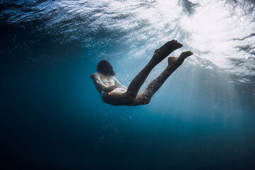 Woman swimming underwater with ocean wave and sun rays.