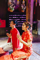 Obraz premium Happy young Asian couple in Chinese traditional dresses praying at temple