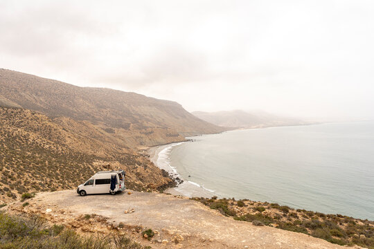 Travelling surfers camp in their van with a dog , campfire and wetsuit, overlooking imsouane, near Tagazout, Agadir, Morocco.