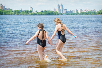 In the summer afternoon on the beach, two girls girlfriends play on the banks of the river.