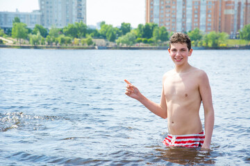 A teenage boy stands in the water in the summer on the beach.