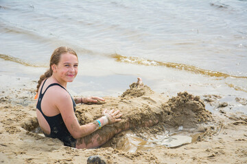 In the summer, a girl sits in the mud on the beach.