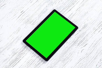 Black tablet with green screen on a wooden table mock up. Copy space chroma key display.