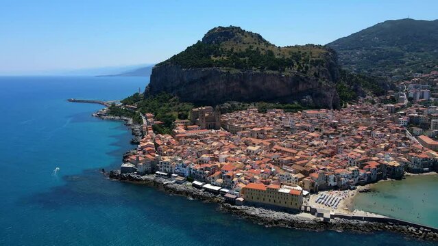 Aerial shot drone flies left as camera pans right from north shore of Cefalu, Sicily, Italy