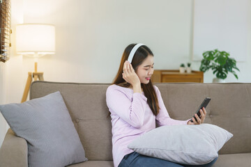 Obraz premium Women sitting on sofa and wearing headphone to listening music on smartphone in lifestyle at home