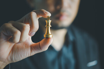 Businessman holding golden king chess in front of silver pawn chess on chessboard for business...