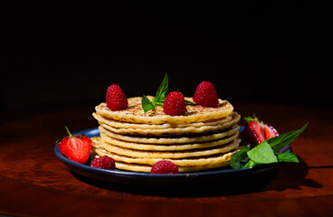 Still life with a plate of delicious pancakes with fresh strawberries and mint leaves over dark background.