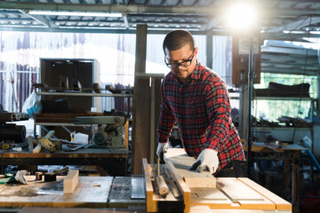 Concentrated Asian carpenter in plaid shirt sawing a long plank in two
