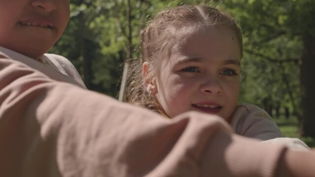Two little girl pulling rope with effort while playing tug-of-war game together outdoors in park