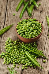 Green peas in closed and open pods, peeled peas in a bowl, scattered pea seeds on a wooden background.