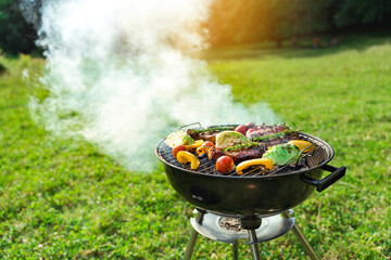 Grilling food in round grill bbq. Grilled meat and vegetables. Picnic outdoors in a meadow.