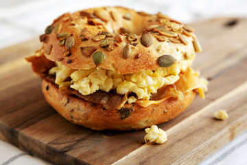 Homemade Bacon, Egg & Cheese Bagel Breakfast Sandwich on a wooden board, side view.