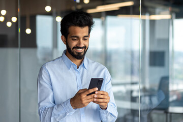 Young successful mature businessman inside the office using the phone, man holding a smartphone online application user, smiling browsing the internet and dialing a call