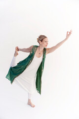 Beautiful blonde Kundalini yoga woman wearing white with a green waistcoat photographed in a white photo studio.  - 619843868