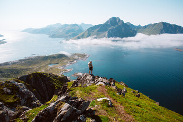 Silhouette of a hiker woman stand on top of mountain hike summit overlooking epic Lofoten Archipelago landscape. Inspiring and amazing idea of adventure. Roadtrip in Norway