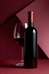 Bottle and glass of red wine on a red background.