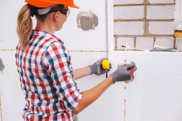 Insulation of the house with polyfoam. The worker is checking with the construction level the...