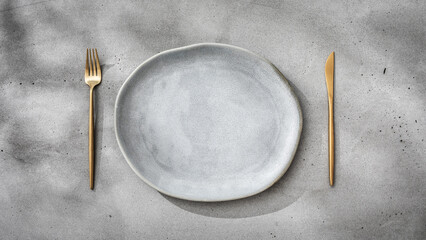 Minimal place setting in gray tones. Gray plate and gold cutlery on concrete table texture