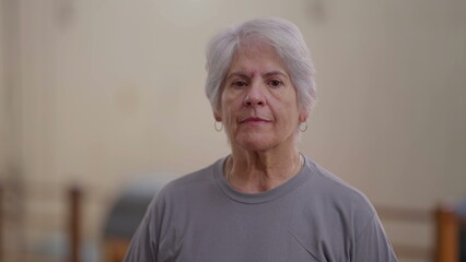 Elderly woman close-up face looking at camera with neutral expression. An older female caucasian person with gray hair