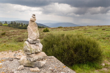 Cairn en pierres de granite sur un sommet et devant un paysage vallonné sous un ciel menaçant d'orage.