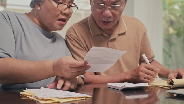 Cropped image of senior couple calculating sum of utility bills sitting at table