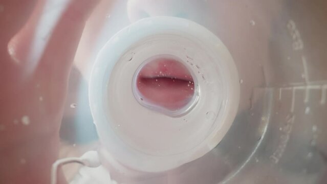 Preschooler drinks clear water from bottle with nipple swallowing actively. Air bubbles appear on waves moving towards mouth macro low angle shot