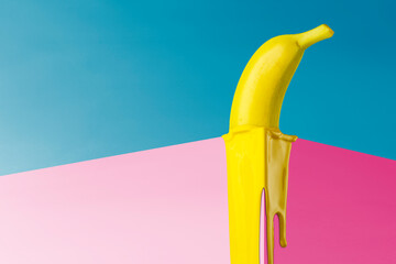 Yellow banana melts on the corner of the pink cube. Creative fruit concept.