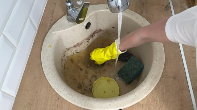 a woman's hand in a yellow glove cleans the sink in the kitchen, the kitchen sink is clogged with food and waste