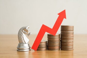 Knight chess and stacked coins as growth profit up graph with red arrow chart on wooden table background. Business strategy tactic, gain investment trading, planning for achieve successful.