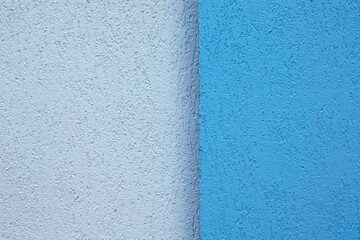 Fragment of the corner of the plastered facade of the building. Converging walls are blue and grey. The surface has a decorative texture. Background.