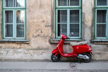 Fototapeta na wymiar Red vintage scooter on the sidewalk in front of an old brick house