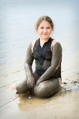 In the summer, a girl sits in the mud on the beach.