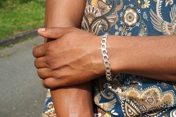 Afrikanischer Mann umfasst Arm mit Hand und silbernem Armband an Handgelenk vor Oberkörper mit...