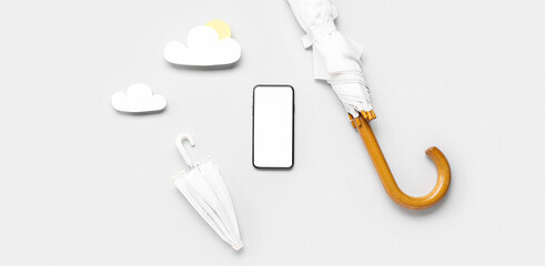 Mobile phone with blank screen, umbrellas and paper clouds on light background. Weather forecast concept